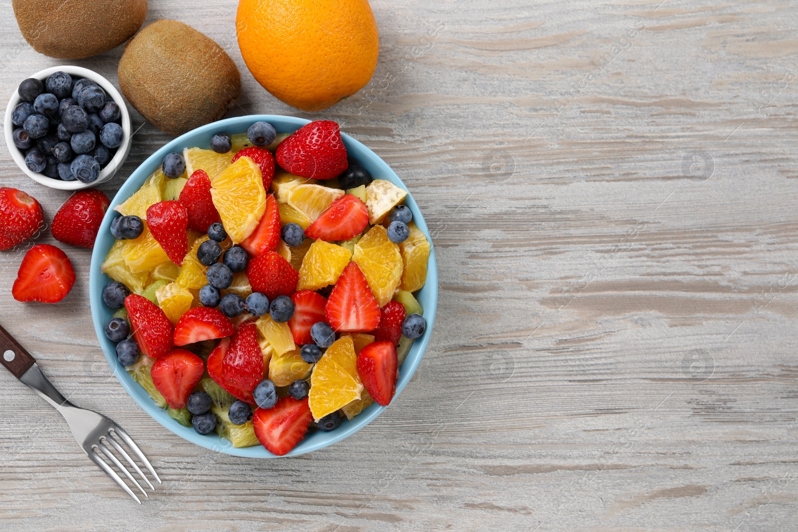 Photo of Delicious fresh fruit salad in bowl served on wooden table, flat lay. Space for text