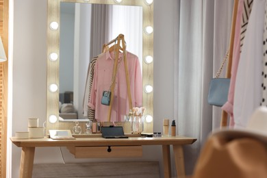 Photo of Makeup room. Stylish mirror and different beauty products on wooden dressing table indoors