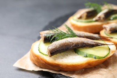 Photo of Delicious sandwich with sprats, cucumbers and dill on slate board, closeup