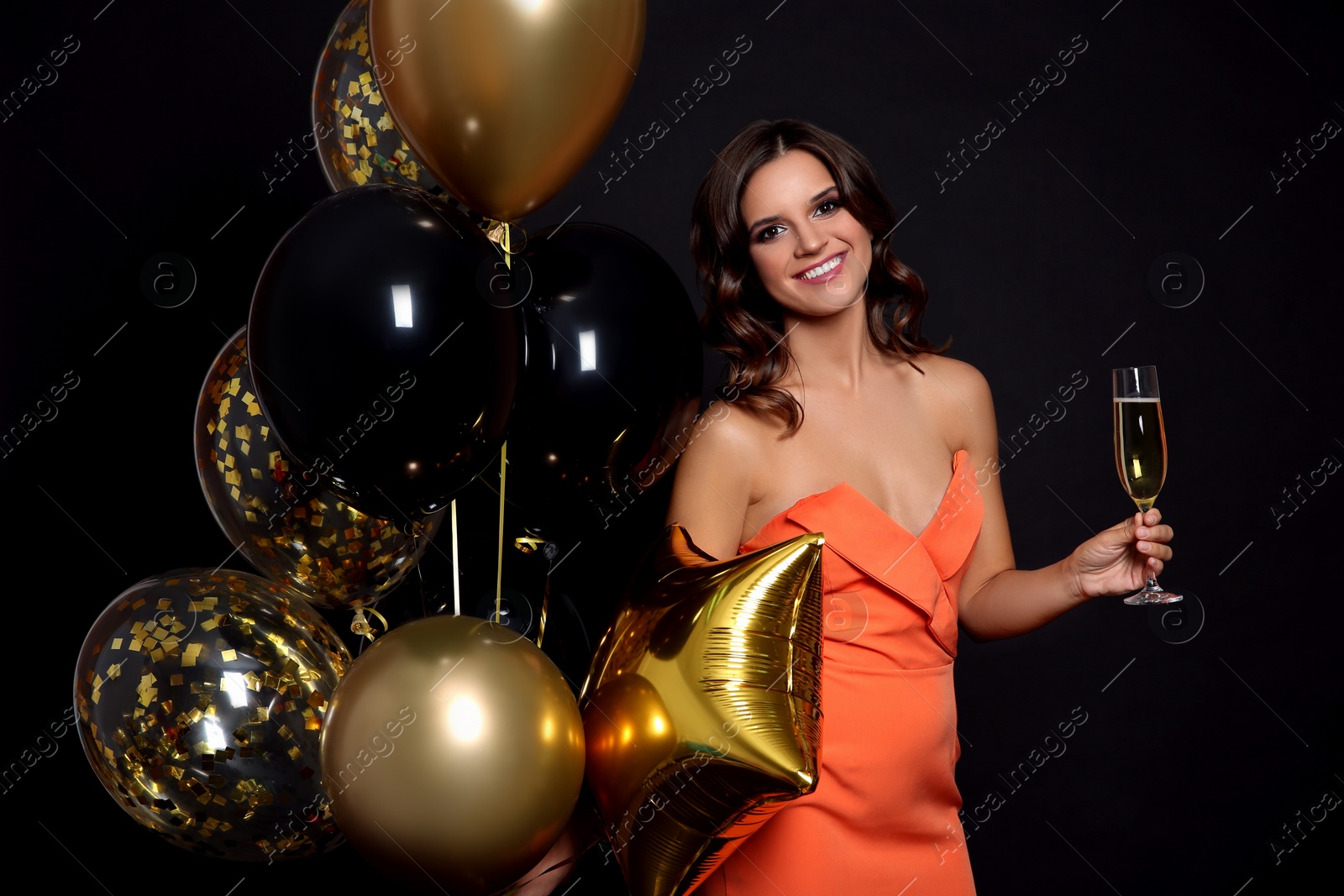 Photo of Happy woman with air balloons and glass of champagne on black background. Christmas party