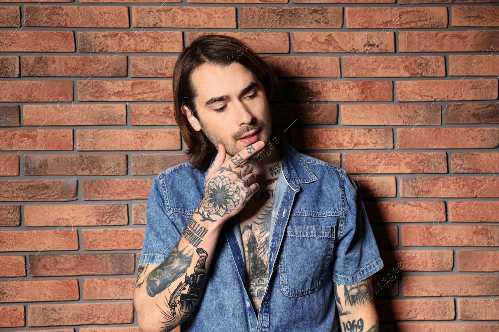 Photo of Young man with tattoos on body near brick wall