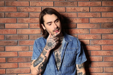 Photo of Young man with tattoos on body near brick wall