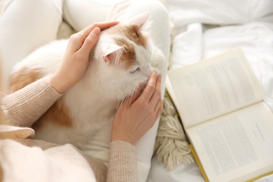 Woman with cute fluffy cat and book on bed, top view
