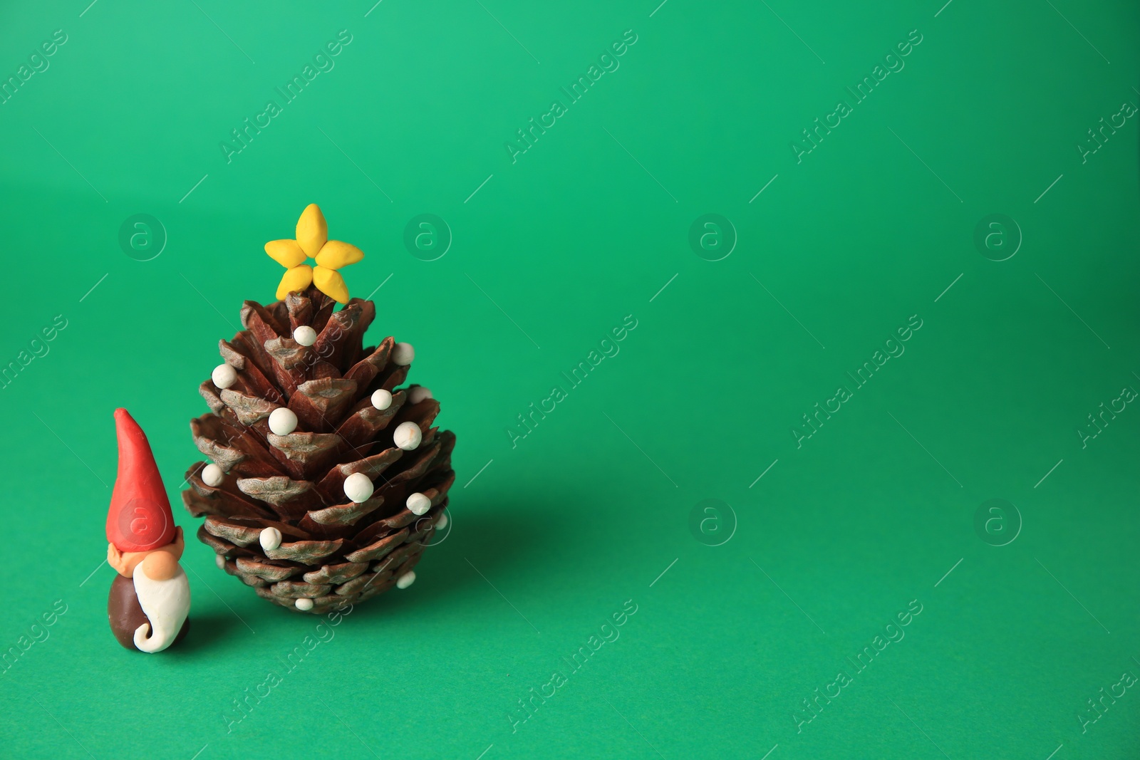 Photo of Beautiful plasticine dwarf with pinecone on green background, space for text. Children's handmade ideas