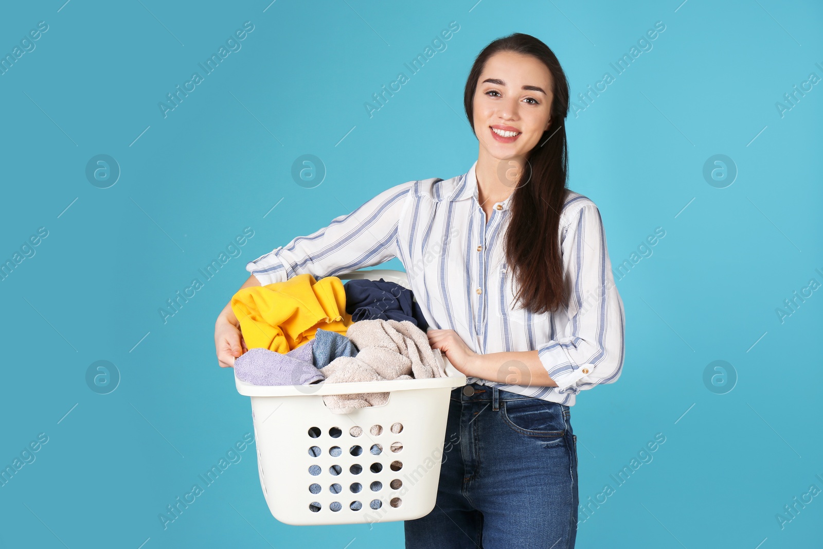 Photo of Happy young woman holding basket with laundry on color background