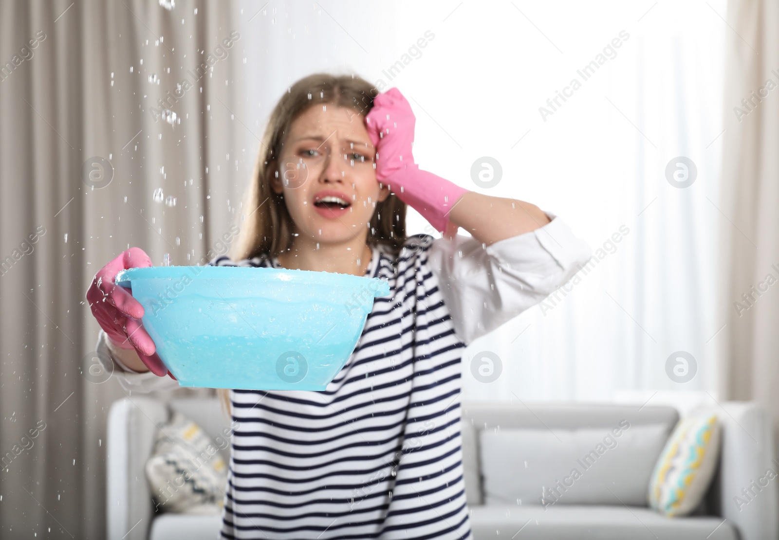 Photo of Emotional young woman collecting water leaking from ceiling in living room. Plumber service