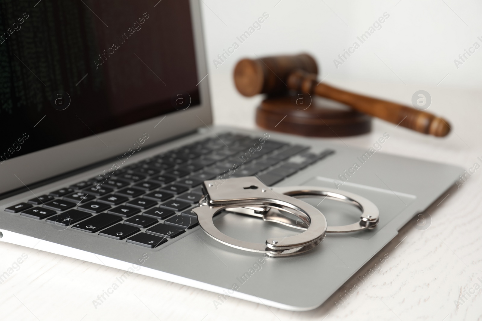 Photo of Laptop, gavel and handcuffs on white table, closeup. Cyber crime