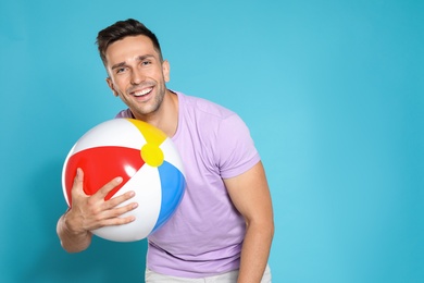 Happy young man with bright inflatable ball on blue background, space for text