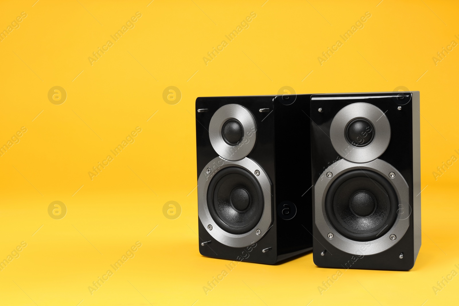 Photo of Modern powerful audio speakers on yellow background, space for text