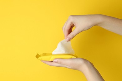Woman taking wet wipe from pack on yellow background, closeup. Space for text