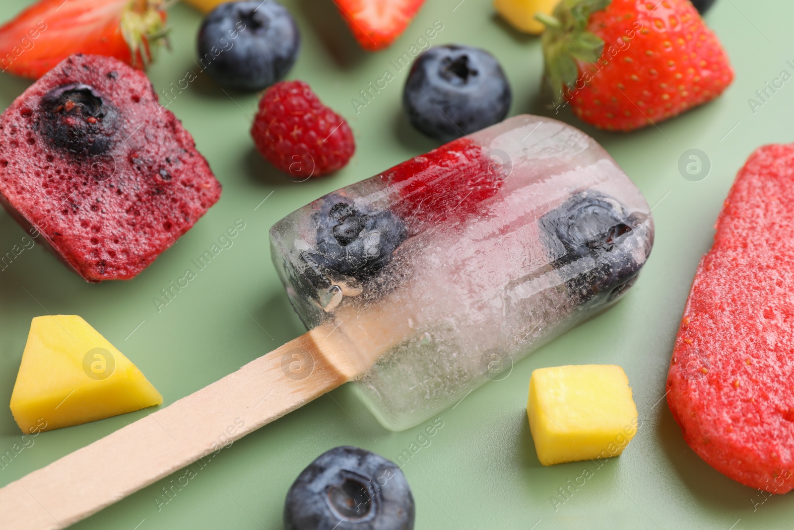 Photo of Tasty fruit ice pops on pale green background, closeup