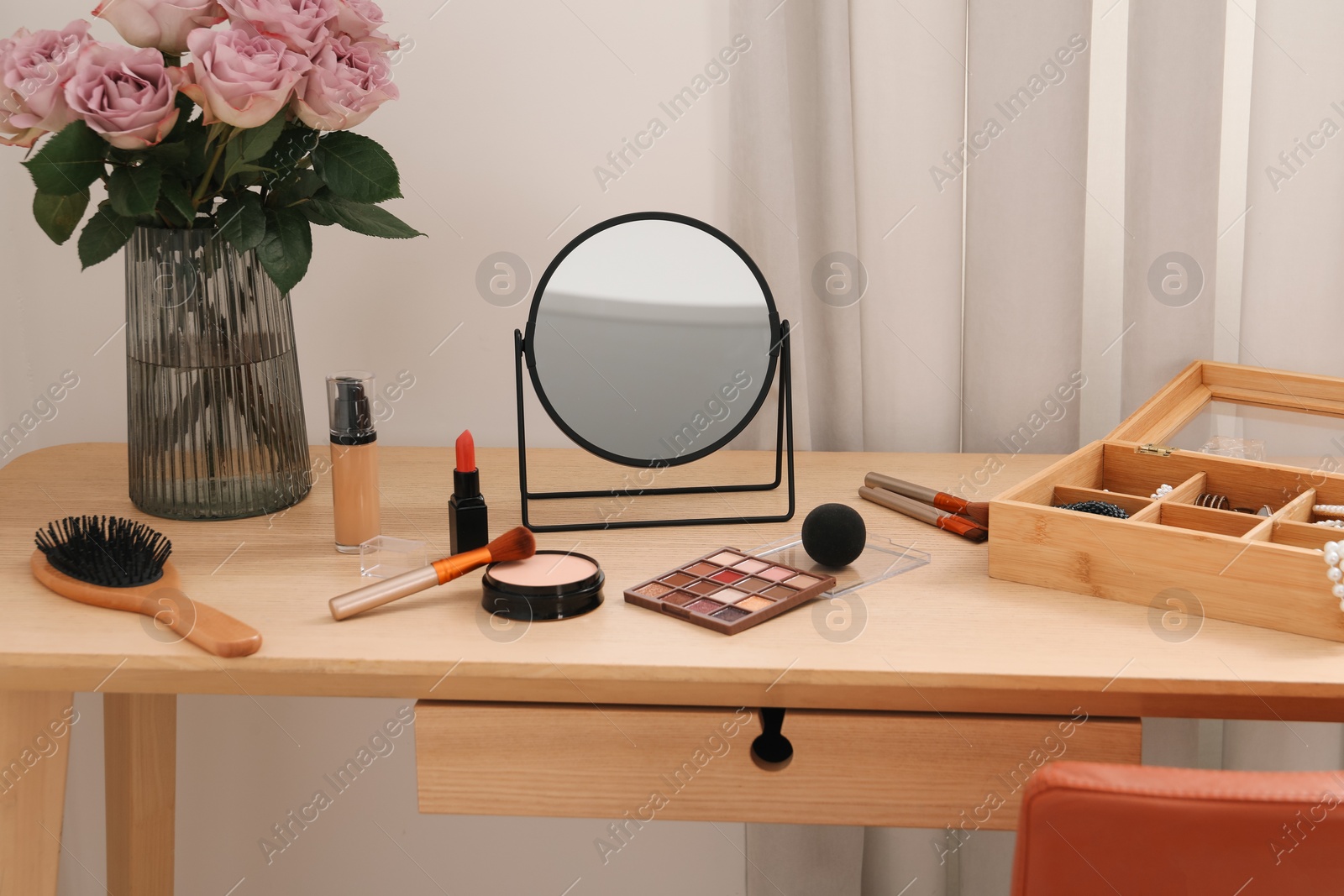 Photo of Mirror, cosmetic products, box of jewelry and vase with pink roses on wooden dressing table in makeup room