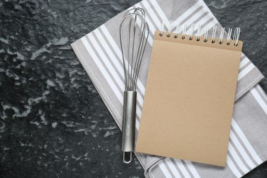 Photo of Blank recipe book and whisk on black textured table, flat lay. Space for text