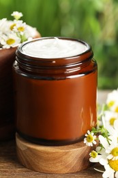 Photo of Jar of hand cream and chamomiles on wooden table, closeup