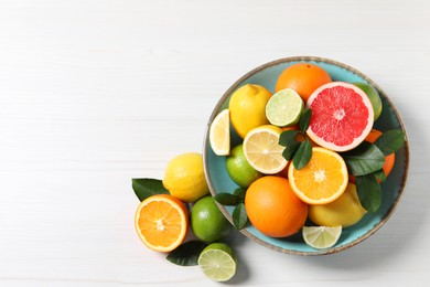 Different cut and whole citrus fruits on white wooden table, top view. Space for text