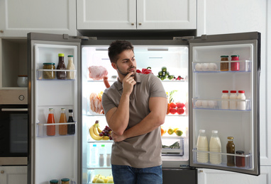 Photo of Thoughtful young man near open refrigerator in kitchen
