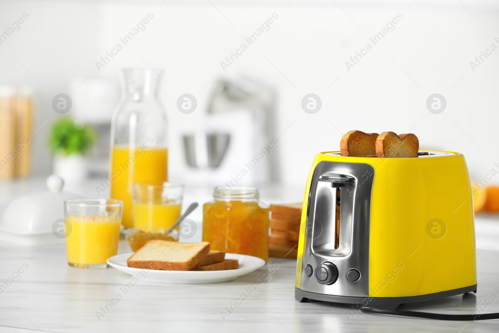 Photo of Yellow toaster with roasted bread slices, jam and glasses of juice on white marble table