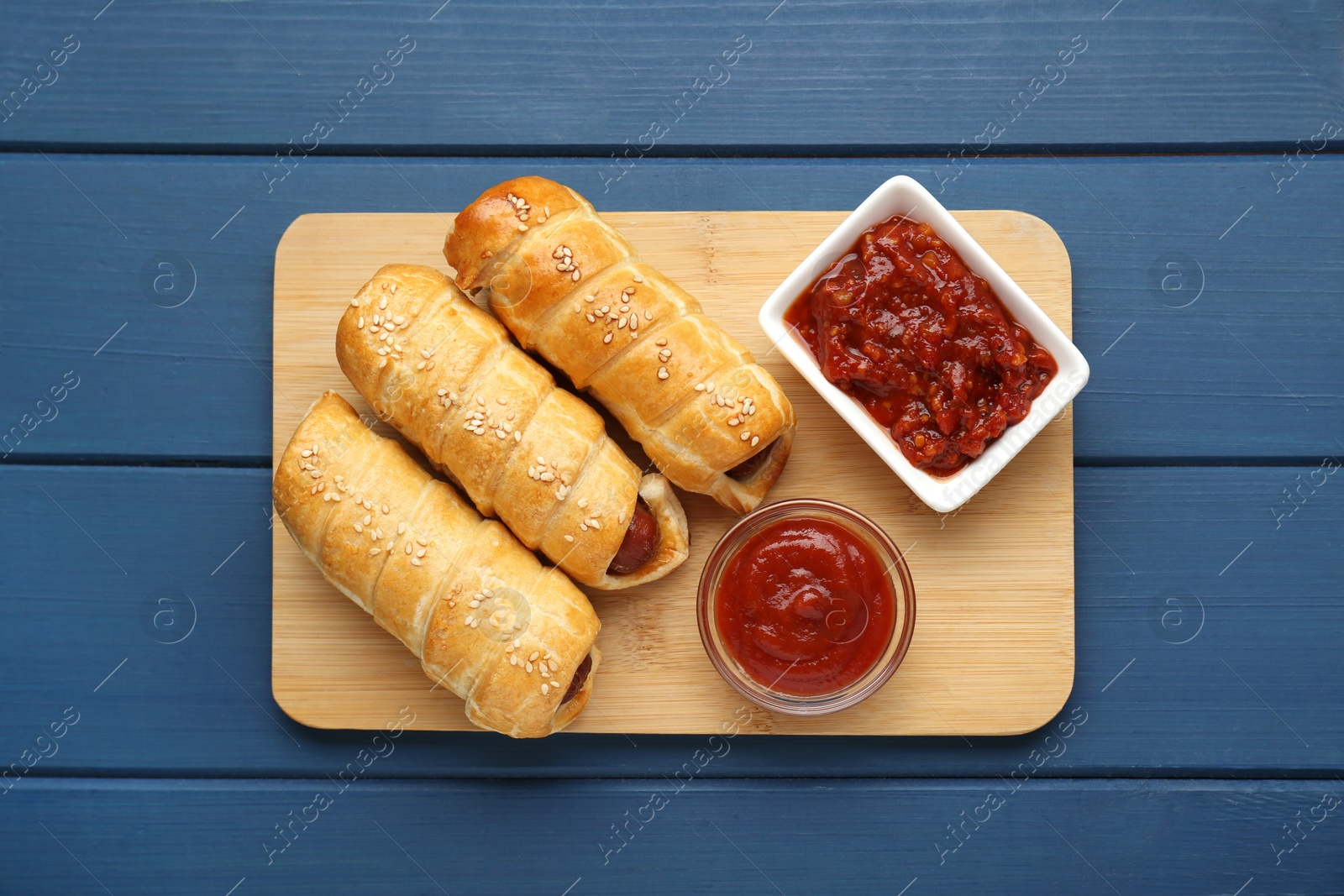 Photo of Delicious sausage rolls and ketchup on blue wooden table, top view