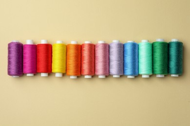 Photo of Set of colorful sewing threads on beige background, flat lay