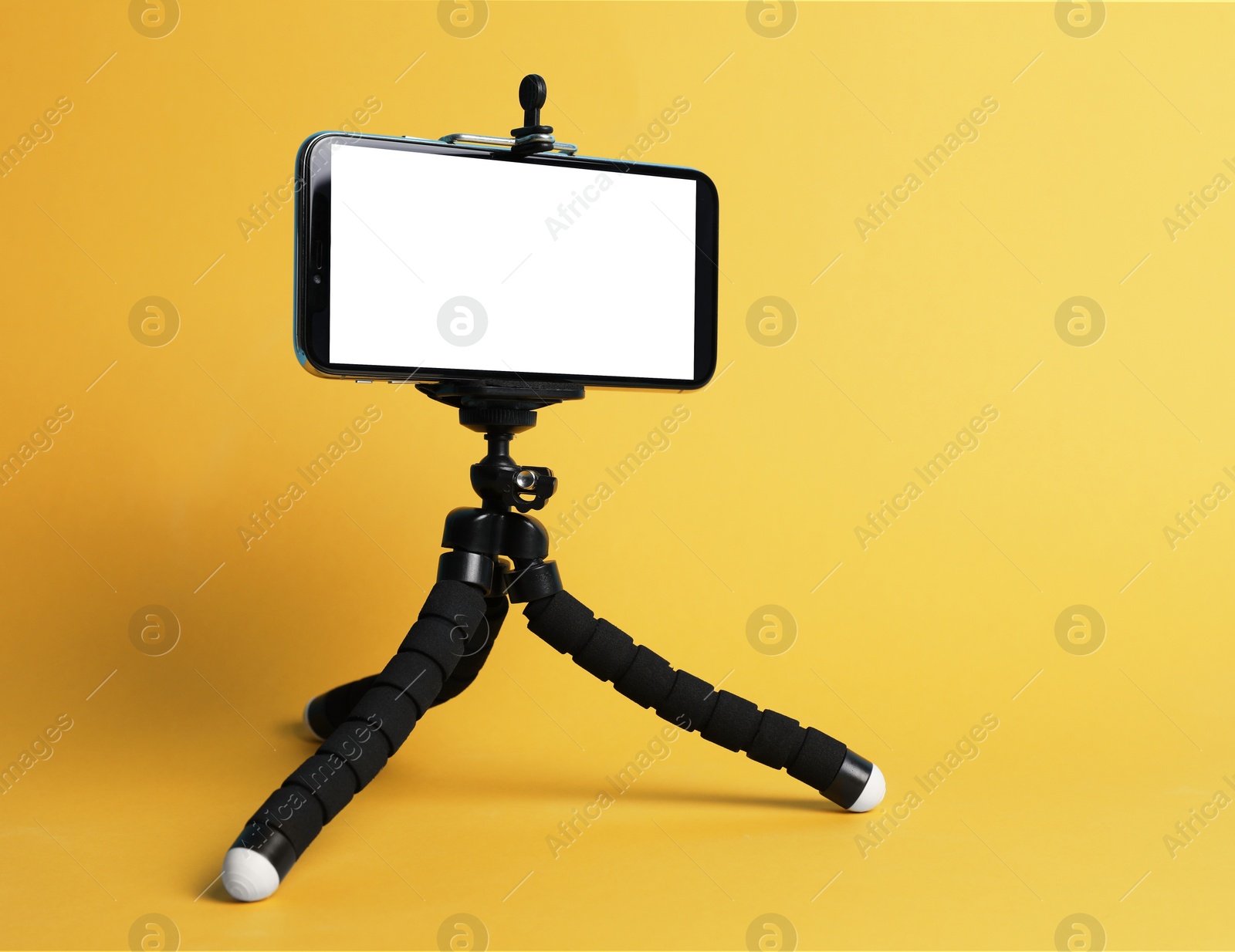 Photo of Modern tripod with smartphone on yellow background. Space for text