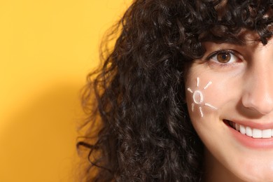 Photo of Beautiful young woman with sun protection cream on her face against orange background, closeup. Space for text