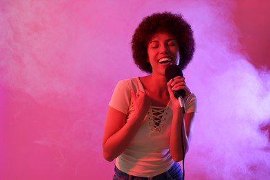Photo of Curly young woman with microphone singing on pink background, space for text. Color tone effect
