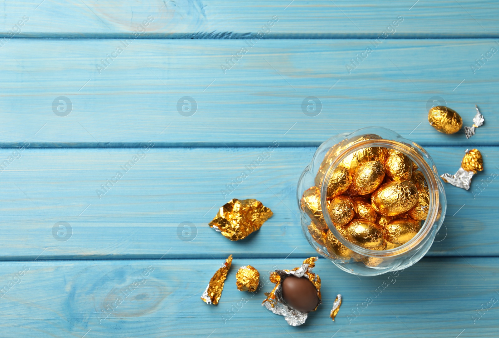 Photo of Chocolate eggs wrapped in golden foil on light blue wooden table, flat lay. Space for text