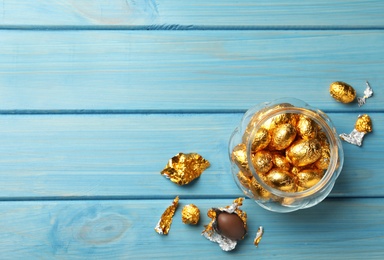 Photo of Chocolate eggs wrapped in golden foil on light blue wooden table, flat lay. Space for text