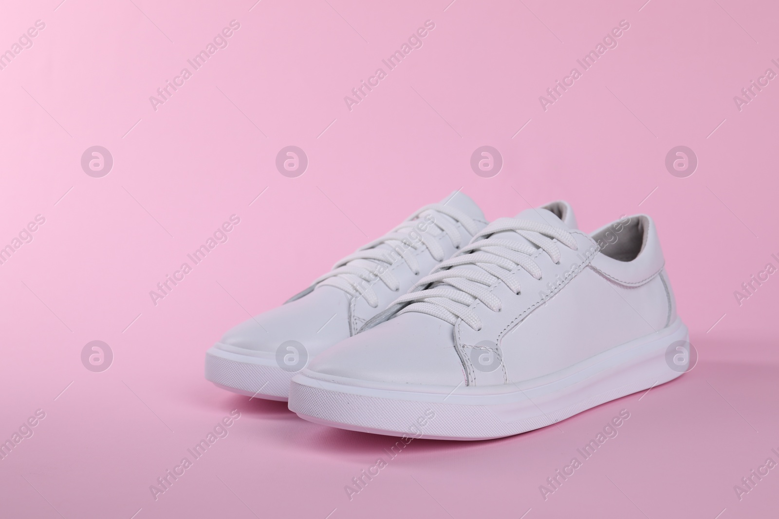 Photo of Pair of stylish white sneakers on pink background