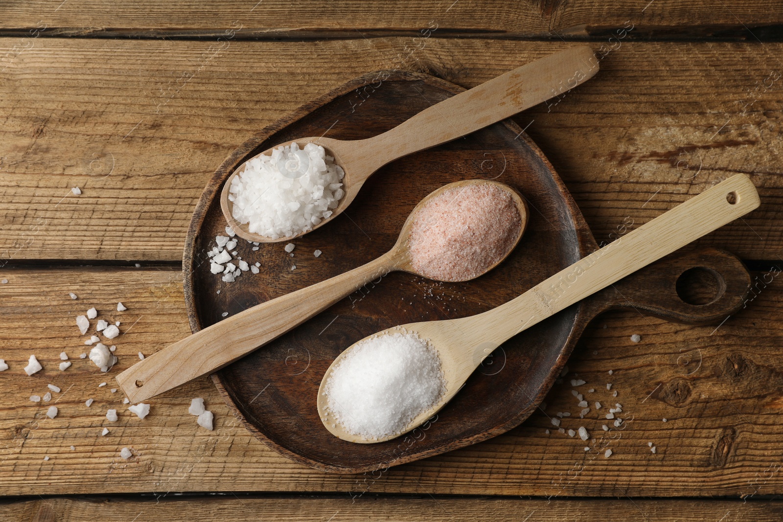 Photo of Different natural salt in spoons on wooden table, flat lay