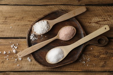 Different natural salt in spoons on wooden table, flat lay