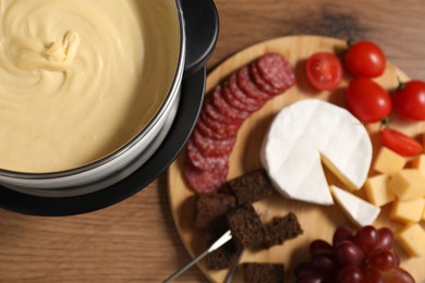 Photo of Fondue with tasty melted cheese, forks and different snacks on wooden table, above view