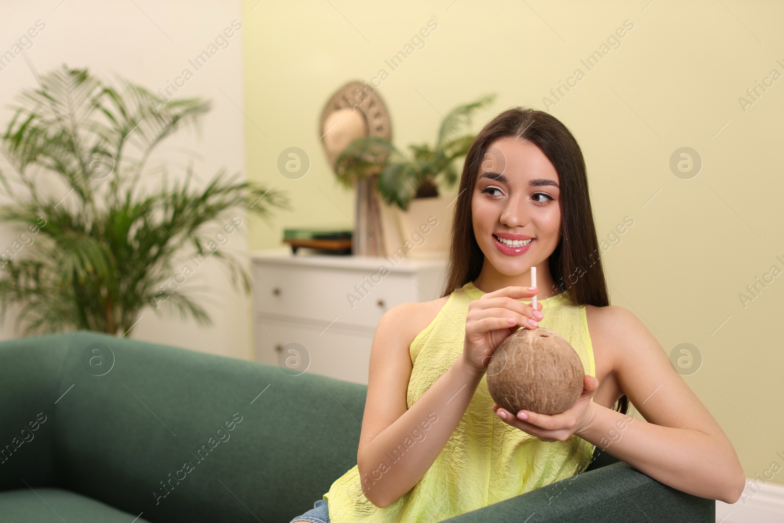 Photo of Young woman with fresh coconut at home, space for text. Exotic fruit