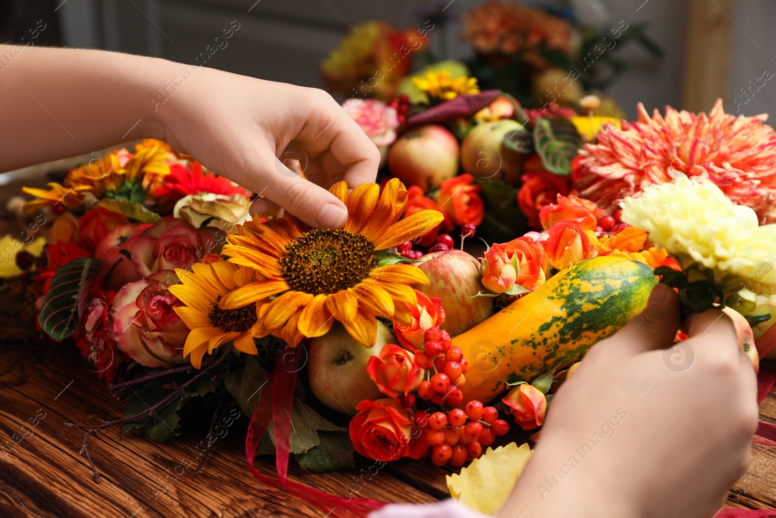 Photo of Florist making beautiful autumnal wreath with flowers and fruits at wooden table, closeup