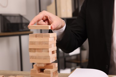 Photo of Playing Jenga. Man building tower with wooden blocks at table indoors, closeup