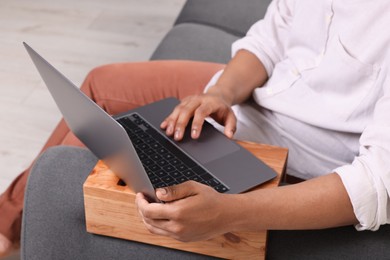 Photo of Man using laptop on sofa armrest wooden table at home, closeup