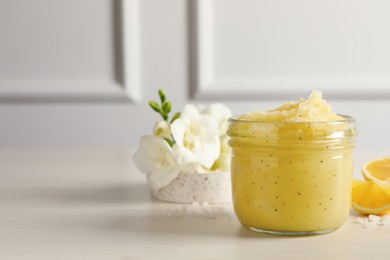 Photo of Body scrub in glass jar, freesia flowers and lemon on light wooden table, space for text