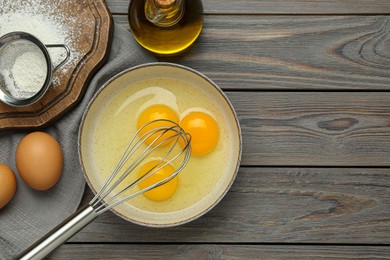 Photo of Whisk, eggs in bowl, oil and flour on wooden table, flat lay. Space for text