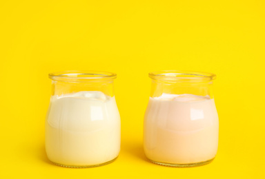 Tasty organic yogurt in glass jars on yellow background