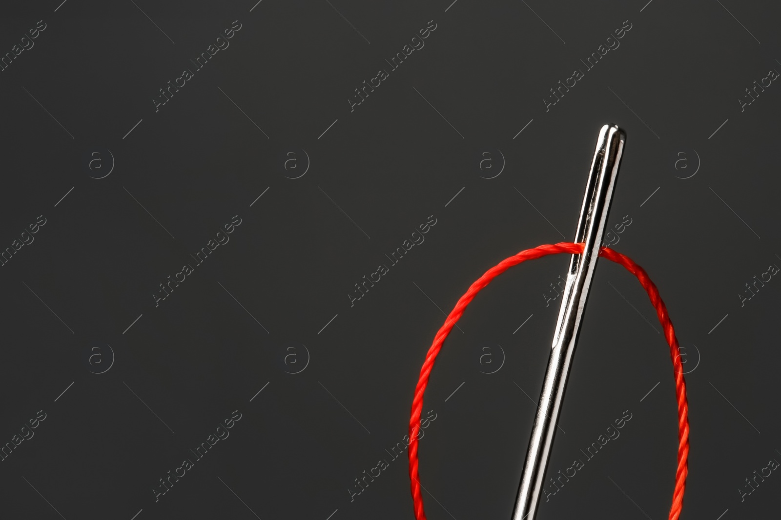 Photo of Needle with sewing thread on dark background, closeup