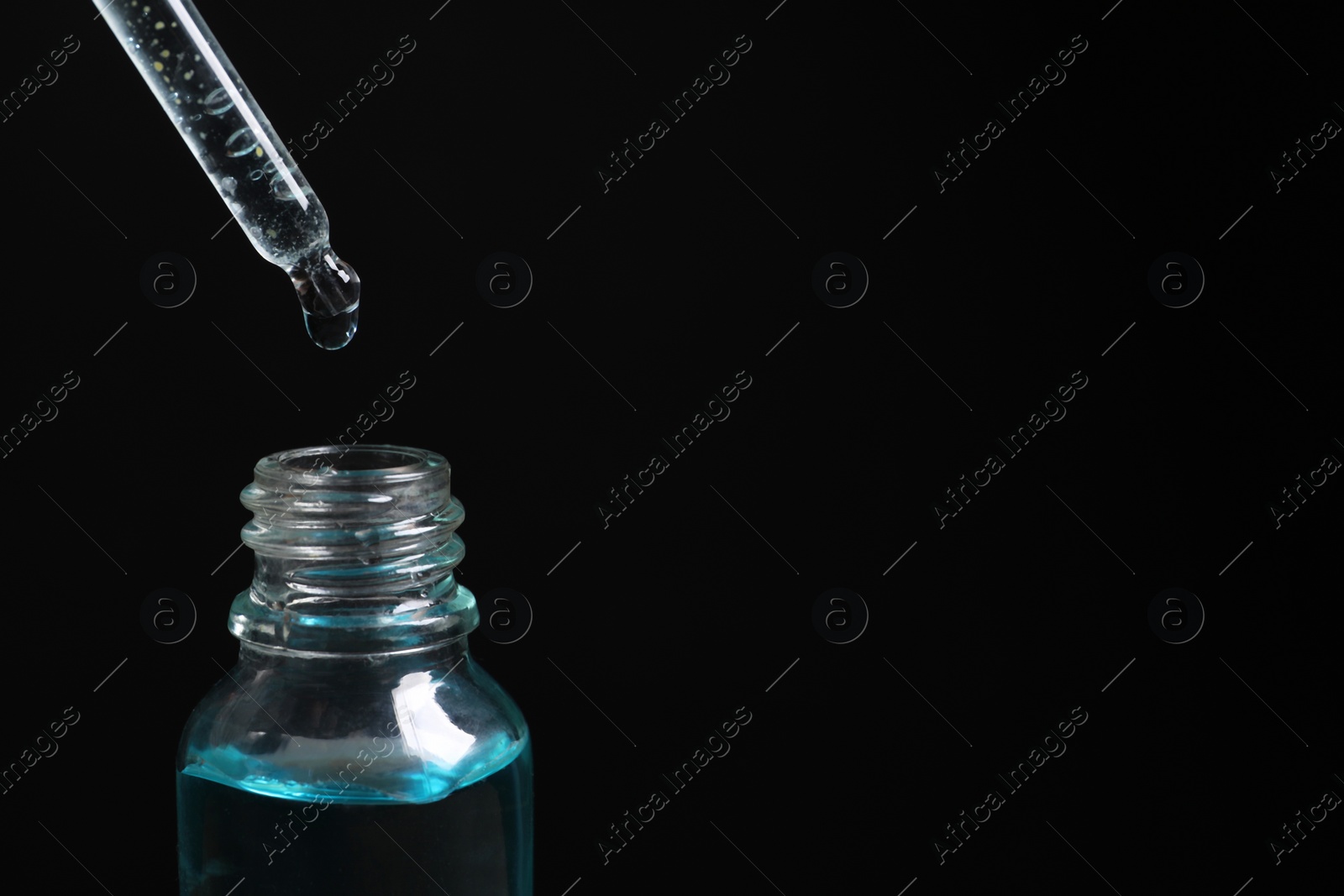 Photo of Dripping cosmetic serum from pipette into bottle on black background, closeup. Space for text