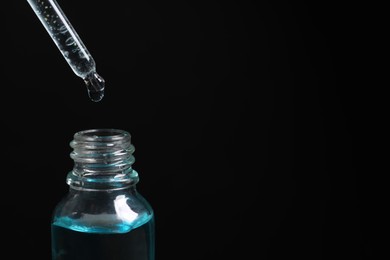 Dripping cosmetic serum from pipette into bottle on black background, closeup. Space for text