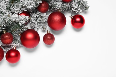 Shiny red Christmas balls and fir tree branches with snow on white background, flat lay. Space for text