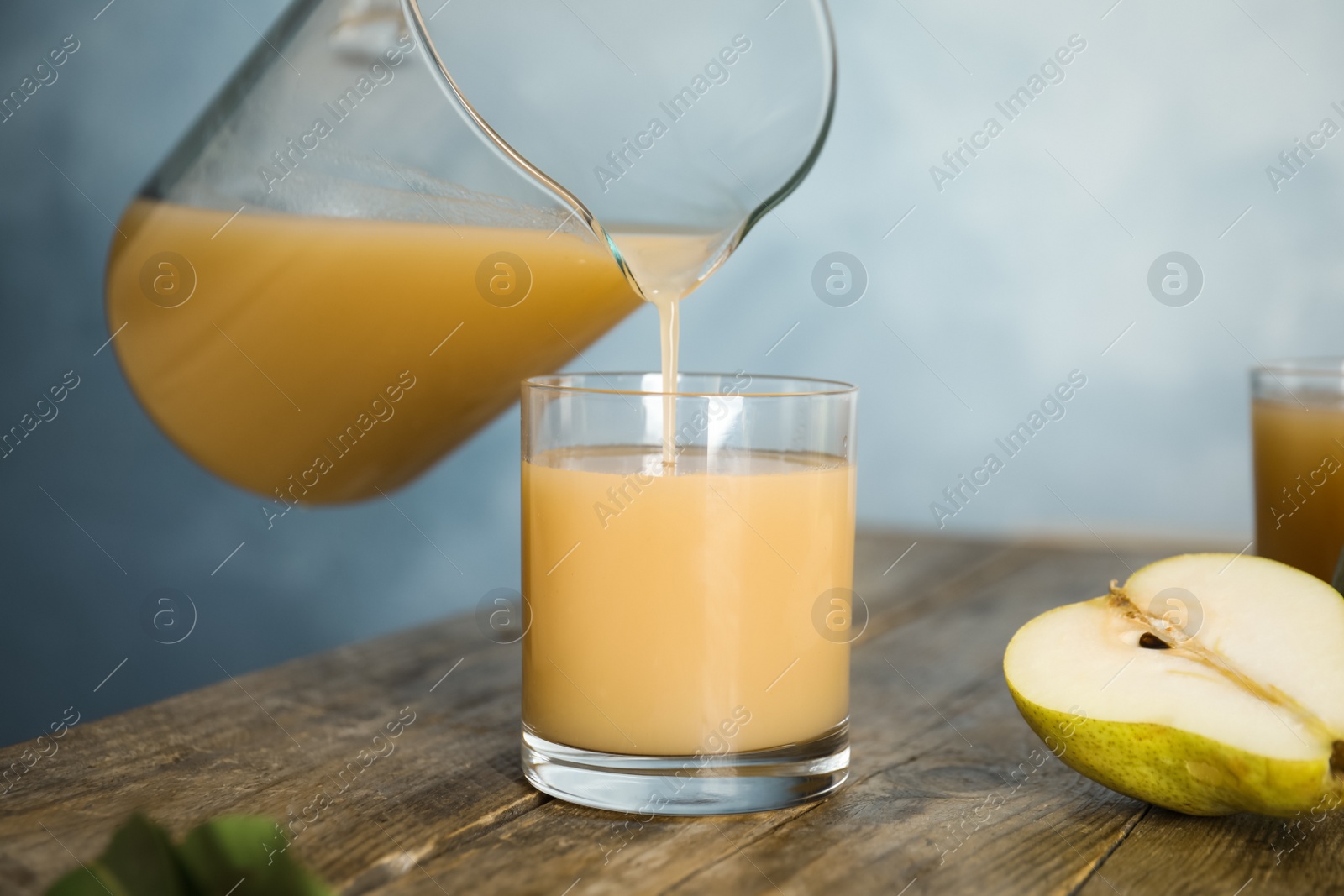 Photo of Pouring tasty pear juice into glass at wooden table, closeup