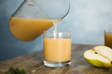 Pouring tasty pear juice into glass at wooden table, closeup