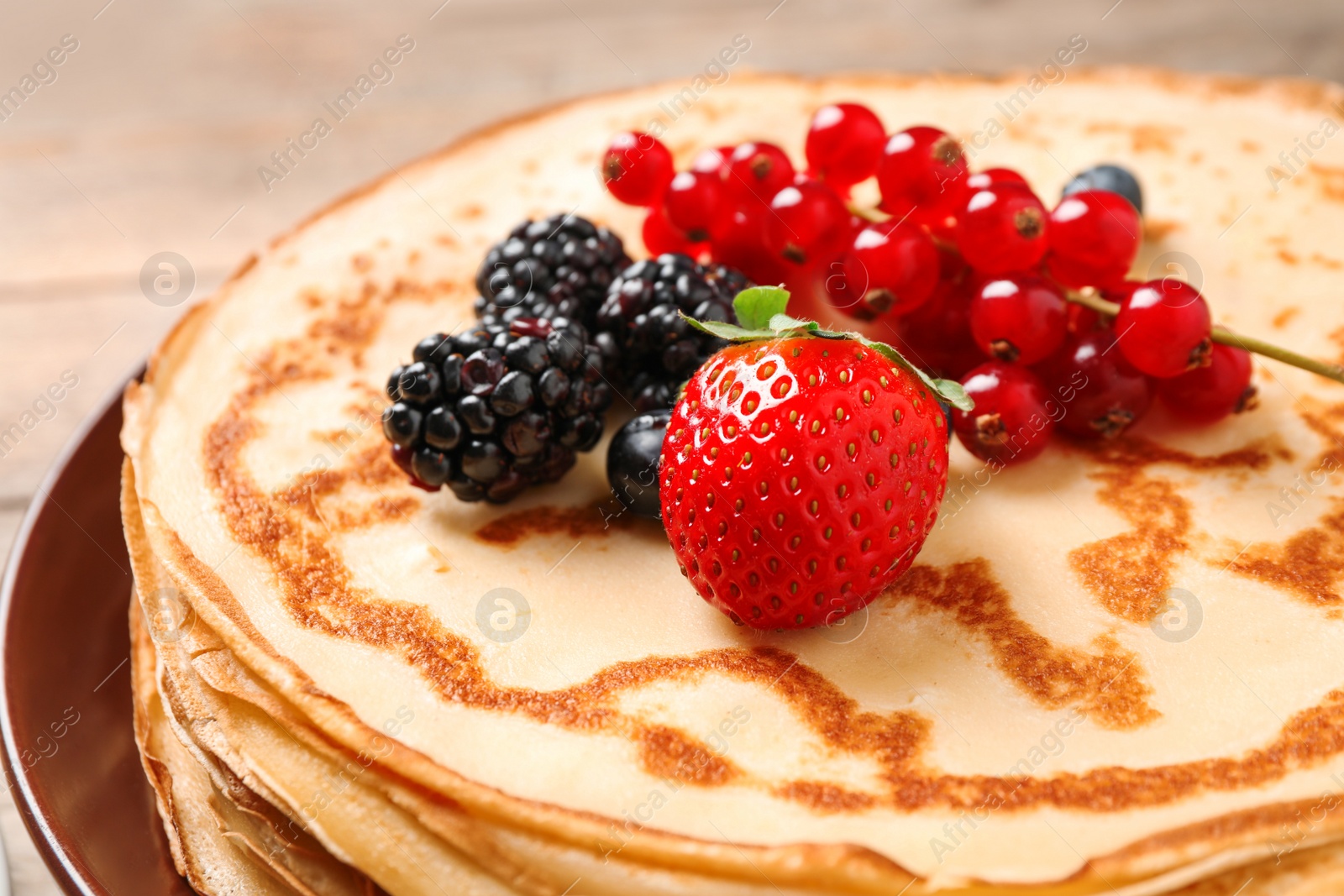 Photo of Delicious thin pancakes with berries on plate, closeup