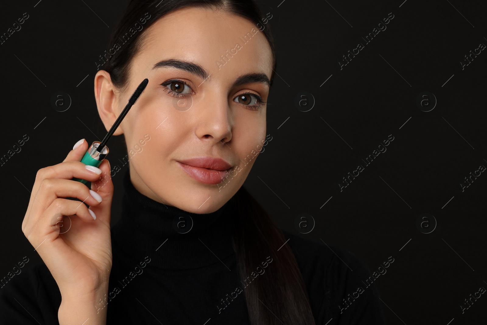 Photo of Beautiful young woman applying mascara on black background, closeup. Space for text