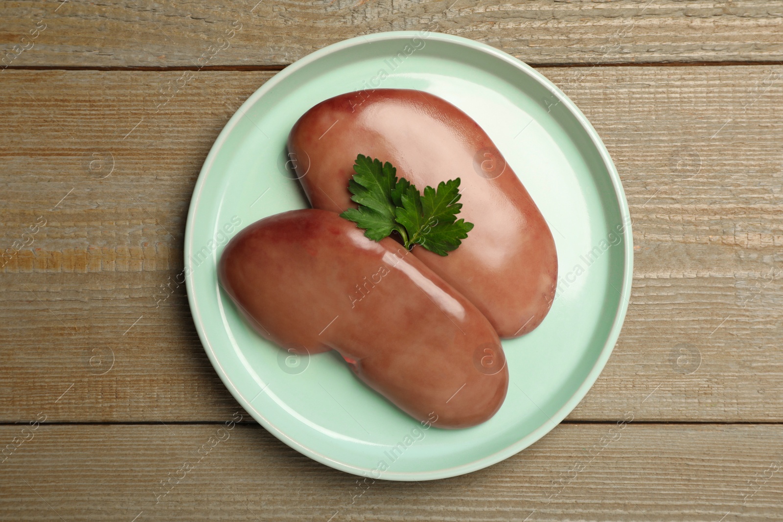 Photo of Fresh raw pork kidneys with parsley on wooden table, top view