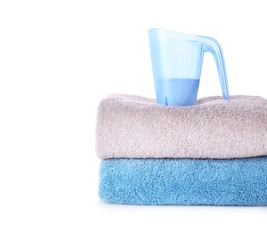 Laundry detergent in plastic measuring cup and towels on white background