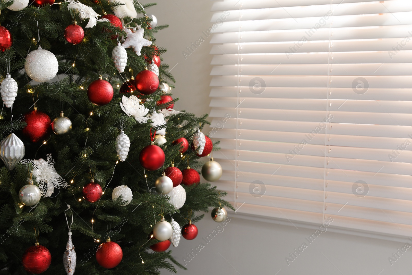 Photo of Beautifully decorated Christmas tree near window indoors. Space for text